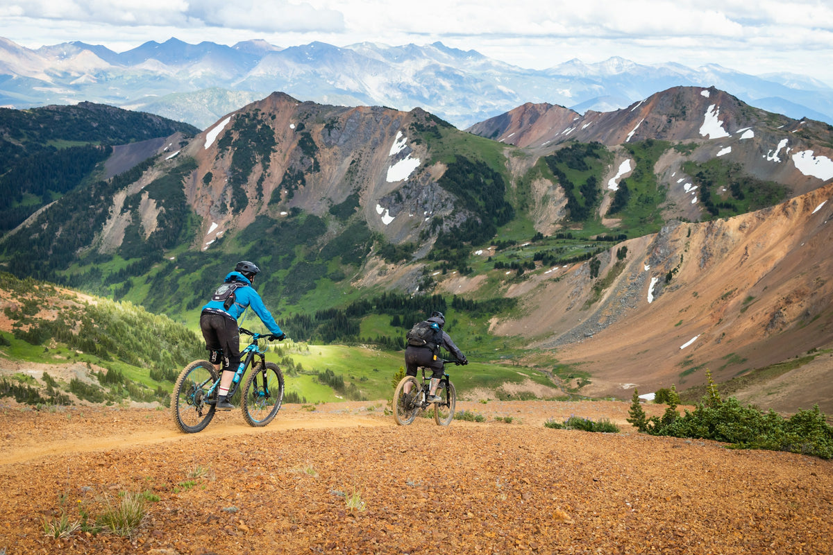Two mountain bikers riding along a trail overlooking mountain peaks